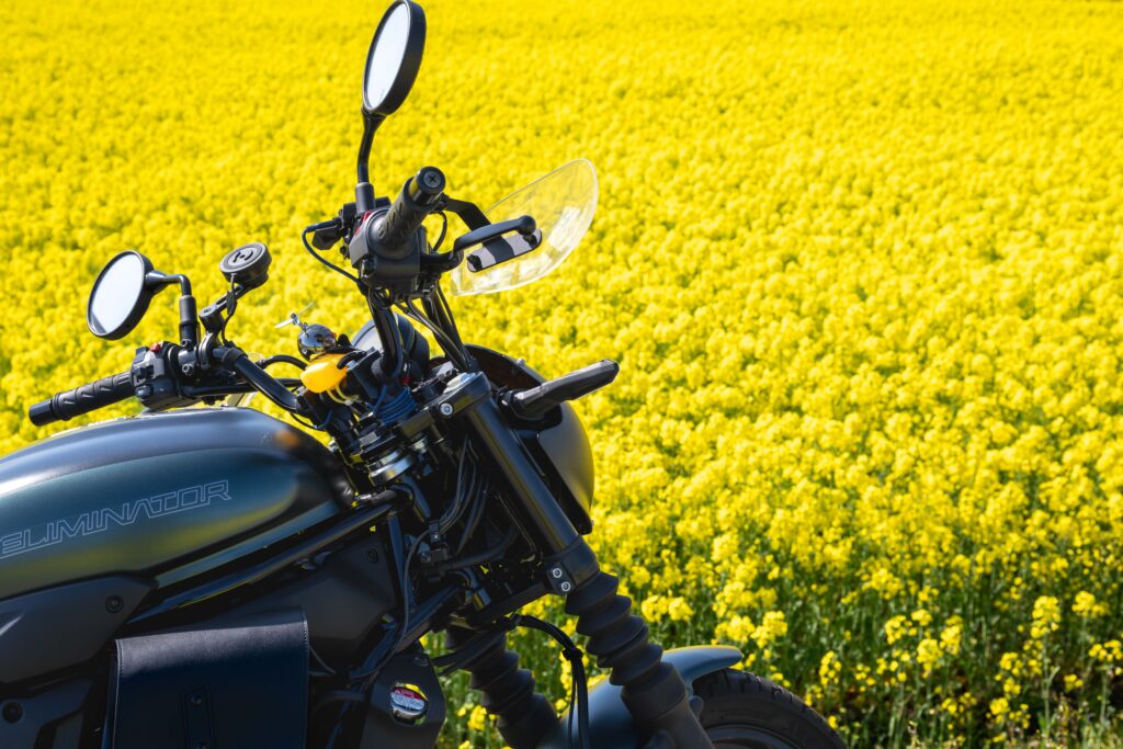 カワサキ エリミネーター400SEのタンクとミラー、ハンドル周辺を菜の花の黄色を
背景に切り取った接写。マットブラック塗装の質感が強調される構図。