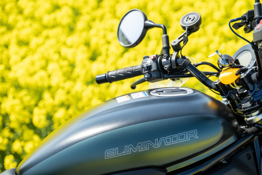カワサキ エリミネーター400SEのタンク右側にあるELIMINATORロゴ。
菜の花の黄色を背景にした接写で、艶消し塗装の質感がよくわかる構図。